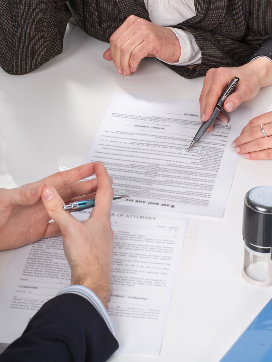 Three people sitting at a table signing documents, hands close-up